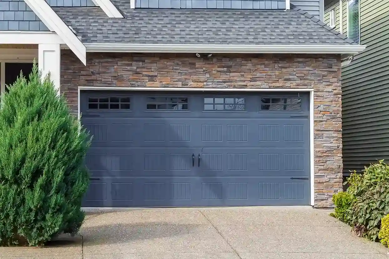 A close-up of a blue paneled garage door with decorative black handles and a row of windows on top.